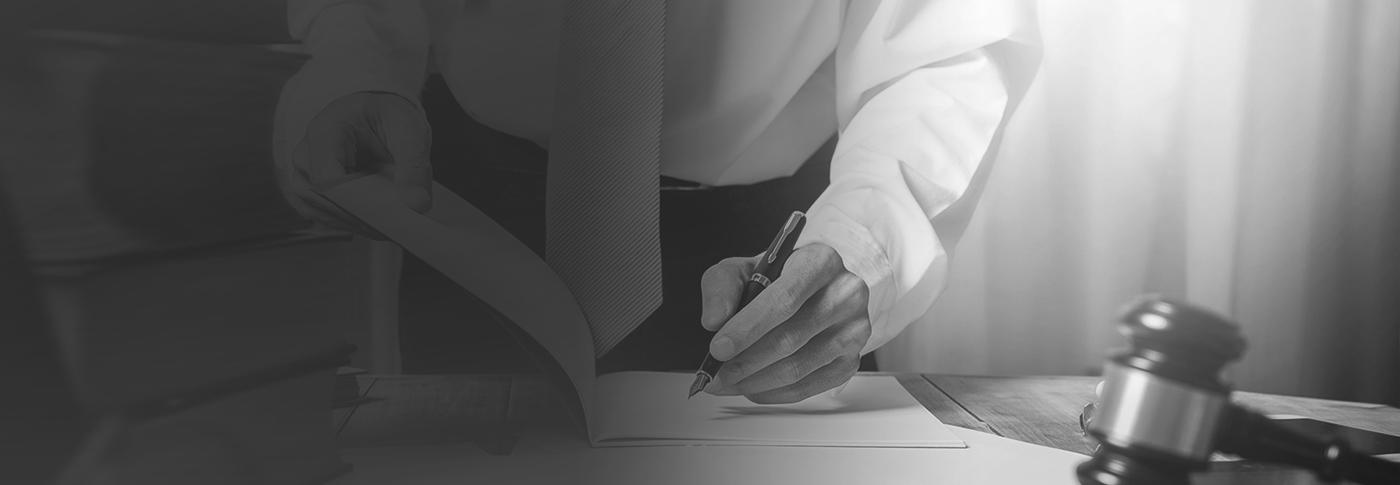 Hand writing with a pen beside a judge's gavel, in black and white